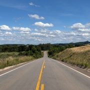 Foto mostra estrada nova, bem no meio da rodovia que segue at&eacute; o infiinito em uma &aacute;rea de mata.O c&eacute;u est&aacute; claro com algumas nuvens. 
