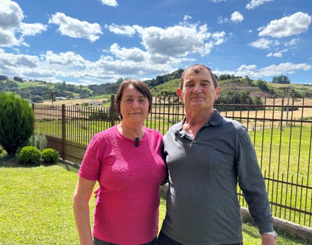 Foto mostra casal abraçados e olhando para a câmera. 