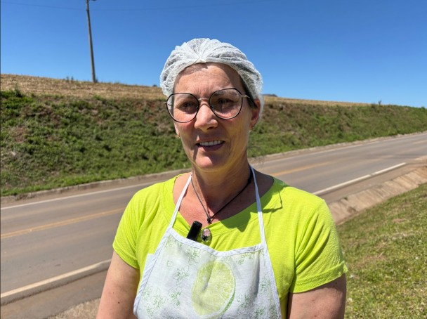 Foto mostra mulher olhando para a câmera, atrás dela a rodovia. Ela está com uma toca higiênica usada em restaurantes. 