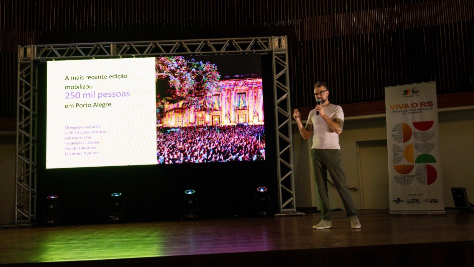 Foto mostra palestrante no palco na frente de um tel&atilde;o.
