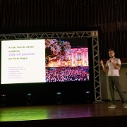 Foto mostra palestrante no palco na frente de um tel&atilde;o.