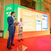 O governador e o vice-governador est&atilde;o posicionados ao lado de um p&uacute;lpito transparente, de frente para uma tela grande que exibe a apresenta&ccedil;&atilde;o &ldquo;Plataforma Clima RS&rdquo;, acompanhada de um QR Code e da interface do sistema mostrada em um dispositivo m&oacute;vel. 