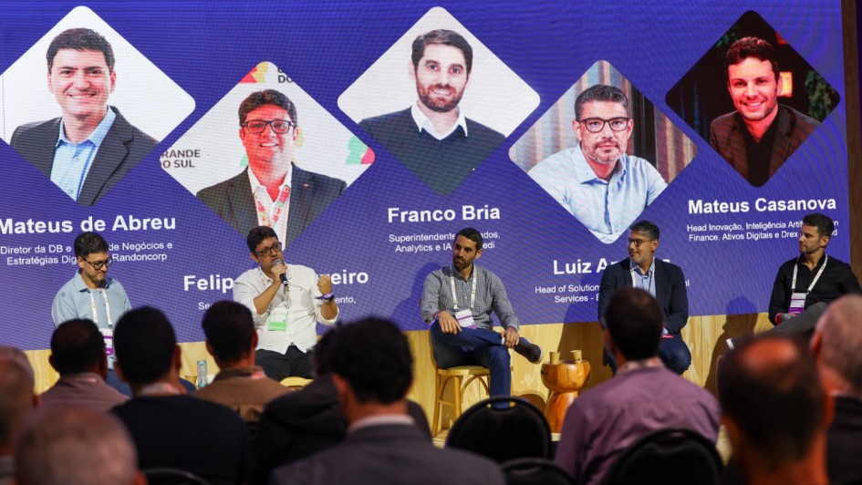 Painel de debate em evento corporativo, com cinco participantes sentados no palco e plateia ao fundo. Um tel&atilde;o azul exibe o tema sobre decis&otilde;es em grandes organiza&ccedil;&otilde;es, com nomes e informa&ccedil;&otilde;es dos painelistas.