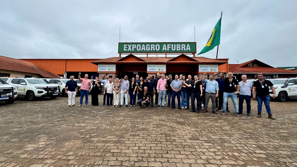 V&aacute;rias pessoas est&atilde;o em p&eacute; lado a lado para foto oficial, em ambos os lados, v&aacute;rios ve&iacute;culos estacionados e, ao fiundo, pavilh&atilde;o com uma bandeira do Brasil e a faixa com os dizeres Expoagro Afubra