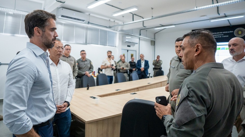 Amplo sagu&atilde;o com v&aacute;rias pessoas, civis e policiais militares. Em primeiro plano, dois homens vestidos de roupas civis conversam com dois homens vestidos de policiais militares, observados por um homem vestido com roupas civis