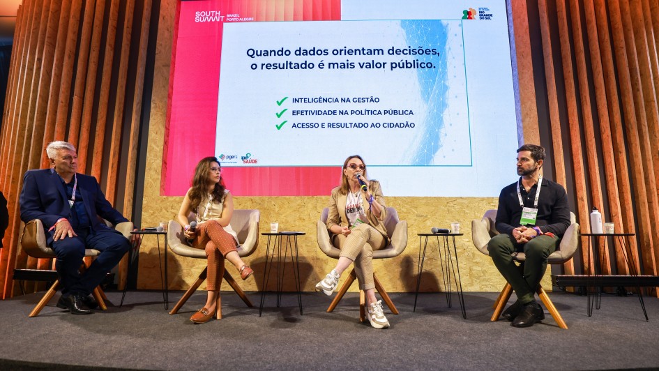 A imagem mostra um painel no South Summit Brazil, com quatro participantes sentados em poltronas diante de um tel&atilde;o grande que exibe o texto: &ldquo;Quando dados orientam decis&otilde;es, o resultado &eacute; mais valor p&uacute;blico&rdquo; acompanhado de tr&ecirc;s t&oacute;picos listados com marcas de sele&ccedil;&atilde;o. 