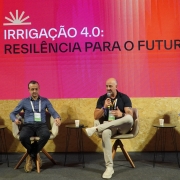 Painel realizado em palco de evento, com quatro participantes sentados em poltronas individuais, cada um com mesa lateral e copo de apoio. Ao fundo, um grande tel&atilde;o exibe o t&iacute;tulo &ldquo;IRRIGA&Ccedil;&Atilde;O 4.0: RESILI&Ecirc;NCIA PARA O FUTURO&rdquo;, com identidade visual em tons de vermelho e laranja.