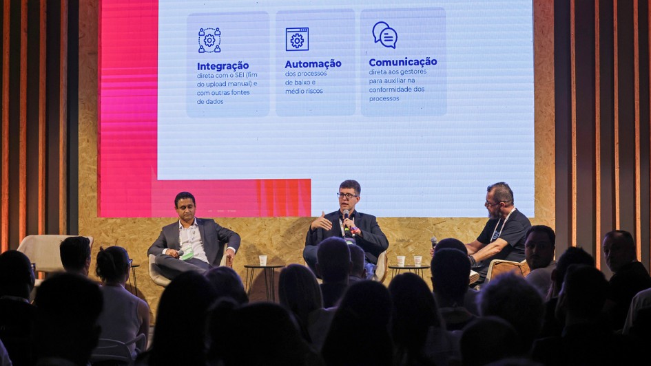 Foto mostra palestrantes sentados diante da plateia.