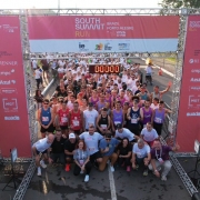 Imagem mostra v&aacute;rias pessoas paradas em um ponto de largada para uma corrida, com um &oacute;rtico, no qual consta a logomarca South Summit Run
