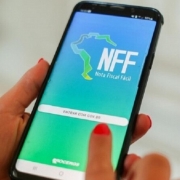 Imagem mostra um celular sendo segurado pela m&atilde;o de uma pessoa, com a imagem da tela aparecendo o aplicativo da Nota Fiscal F&aacute;cil