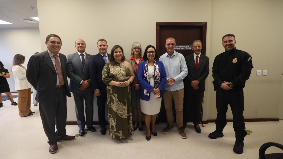 A foto registra um grupo alinhado em frente &agrave; porta da Central Integrada de Alternativas Penais. As pessoas est&atilde;o organizadas lado a lado em ambiente interno de paredes claras.