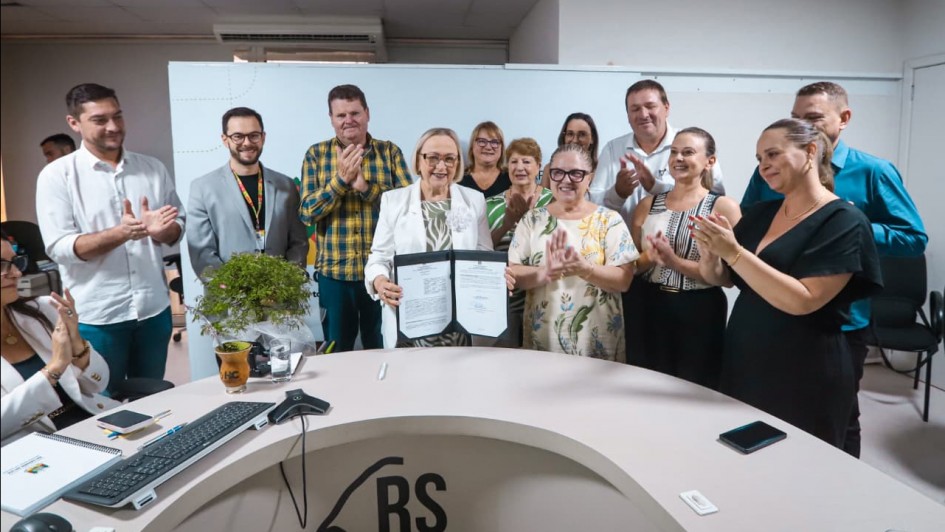 Foto mostra secret&aacute;ria Arita Bergmann com um documento nas m&atilde;os e outras pessoas posando ao lado dela aplaudindo o ato.