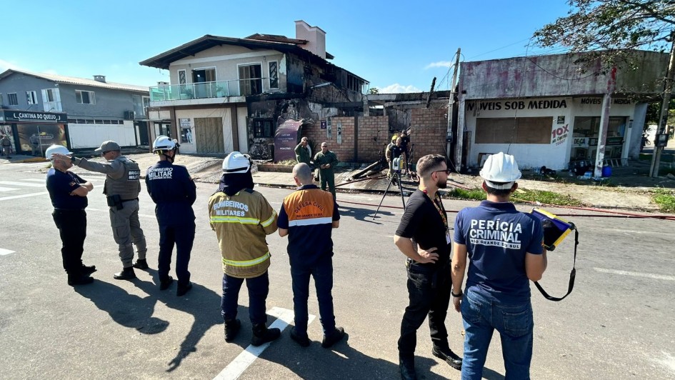 Um grupo de sete pessoas sob uma lona observa uma casa com avarias em sua fachada