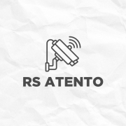 Fundo claro com textura que lembra papel amassado. No centro, h&aacute; um &iacute;cone de uma c&acirc;mera de vigil&acirc;ncia inclinada, com tr&ecirc;s linhas curvas ao lado indicando que est&aacute; transmitindo ou detectando movimento. Abaixo do &iacute;cone, est&aacute; escrito em letras grandes e escuras: &ldquo;RS ATENTO&rdquo;.
