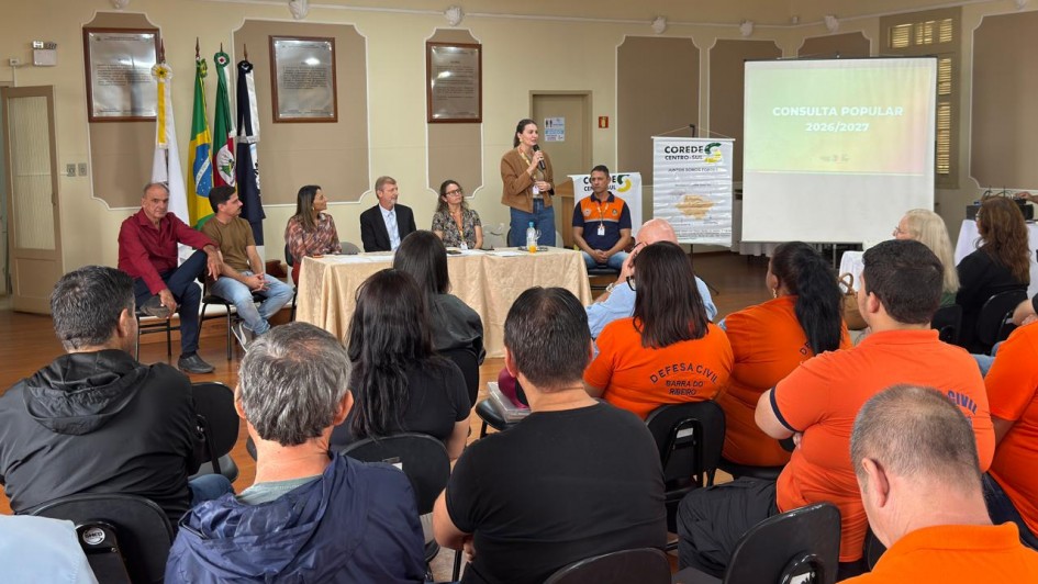 Foto mostra assembleia da Consulta Popular com uma mulher falando em p&eacute; diante da plateia.