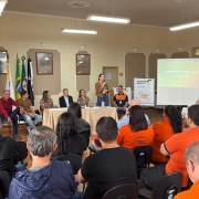 Foto mostra assembleia da Consulta Popular com uma mulher falando em p&eacute; diante da plateia.