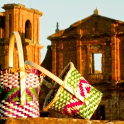 Foto mostra cestos com arte ind&iacute;gena em primeiro plano e ao fundo a fachada das ru&iacute;nas de S&atilde;o Miguel.