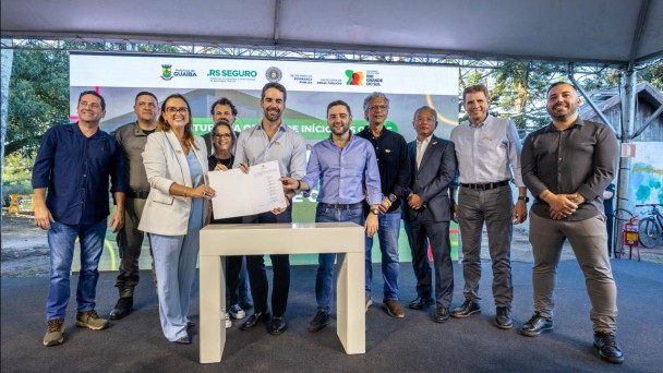 Foto mostra o governador Eduardo Leite e a prefeita segurando um documento. O vice-governador Gabriel Souza e outras autoridades acompanham o ato.