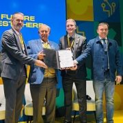 Foto mostra quatro homens segurando o documento assinado no palco da feira. 
