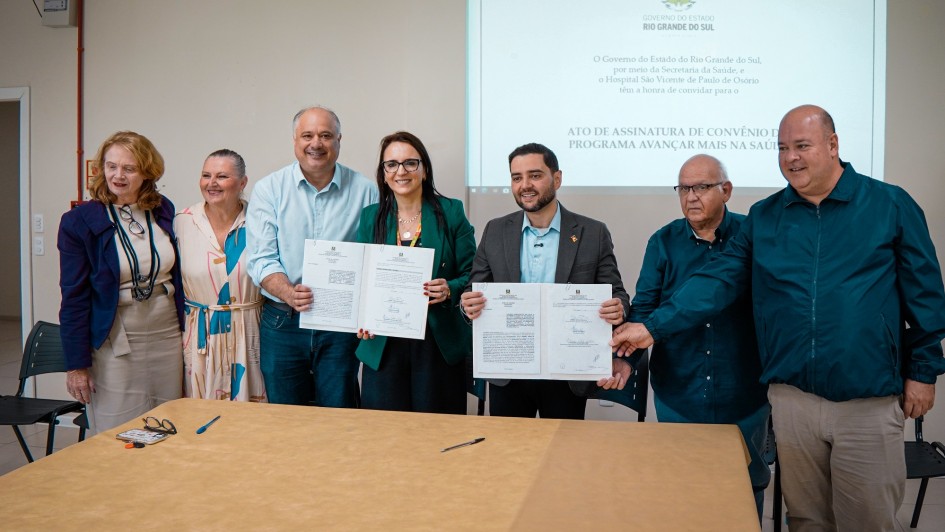 Foto mostra o vice-governador Gabriel Souza e a secret&aacute;ria da Sa&uacute;de, Lisiane Fagundes seguram o documento do conv&ecirc;nio, e outras pessoas segurando os documentos assinados; 