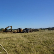 Foto mostra campo onde est&aacute; sendo feita a obra. Ao fundo m&aacute;quinas trabalham no terreno. Em primeiro plano, uma placa do governo do Estado sobre a obra.