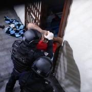 Esta &eacute; uma descri&ccedil;&atilde;o da imagem "Pol&iacute;cia Penal do RS participa de nova fase de opera&ccedil;&atilde;o contra comunica&ccedil;&otilde;es il&iacute;citas em apoio &agrave; estrat&eacute;gia nacional.jpeg" para fins de acessibilidade:

A fotografia em plano m&eacute;dio captura um policial penal de costas, em meio a uma galeria prisional vazia.

O Policial: Posicionado no centro-direita do quadro, o policial veste o uniforme operacional preto. Nas costas de sua camiseta, destaca-se a inscri&ccedil;&atilde;o "POL&Iacute;CIA PENAL" em letras brancas grandes, com a frase "RIO GRANDE DO SUL" logo abaixo em letras amarelas menores. Ele utiliza um cintur&atilde;o t&aacute;tico preto completo com diversos acess&oacute;rios.

O Ambiente:

O policial caminha ou observa um corredor longo e estreito de uma galeria prisional.

&Agrave; esquerda, estende-se uma sequ&ecirc;ncia de portas de celas feitas de grades de ferro pintadas de amarelo, todas fechadas.

O ch&atilde;o &eacute; de concreto cinza e as paredes s&atilde;o de blocos de concreto aparentes.

A ilumina&ccedil;&atilde;o &eacute; artificial, vinda de l&acirc;mpadas no teto, criando um contraste de luz e sombra ao longo do corredor.

A imagem reflete uma atmosfera de seguran&ccedil;a, fiscaliza&ccedil;&atilde;o e rotina operacional dentro de um estabelecimento prisional.
