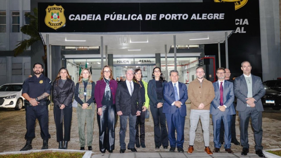 Foto mostra comitiva com o ministro e o secret&aacute;rio na frente da unidade prisional. Ao fundo est&aacute; escrito "Cadeia P&uacute;blica de Porto Alegre" e o bras&atilde;o da Pol&iacute;cia Penal.