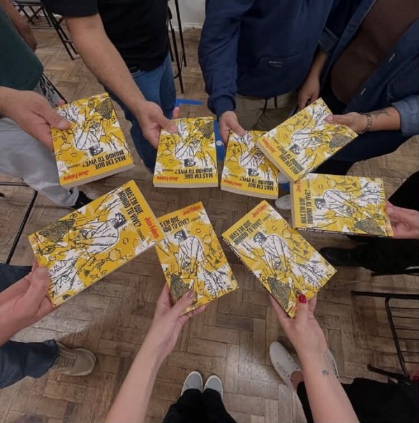 Foto mostra um grupo em roda com livros na mão. A foto mostra apenas as mãos e os livros.