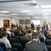 A imagem mostra um audit&oacute;rio lotado e a secret&aacute;ria do Meio Ambiente e Infraestrutura posicionada em p&eacute; no palco, falando ao microfone. 
