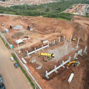 Imagem a&eacute;rea de obras em um amplo terreno vazio, com colunas de concreto j&aacute; erguidas e v&aacute;rias m&aacute;quinas trabalhando no terreno