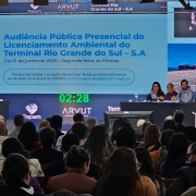 Foto mostra a mesa do evento com plateia assistindo.