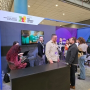 Foto mostra estande da Sict com participantes conversando.
