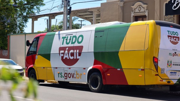 Foto mostra a Unidade M&oacute;vel Tudo F&aacute;cil, um &ocirc;nibus colorido nas cores amarelo, verde e vermelho, com a marca do programa num fundo branco.