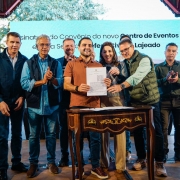 V&aacute;rias pessoas est&aacute; em p&eacute; atr&aacute;s de uma pequena mesa, segurando um documento assinado