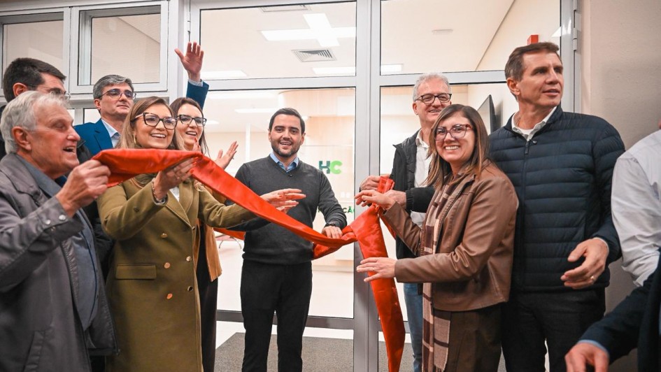 Grupo de pessoas em ambiente interno corta uma fita vermelha na entrada de um espa&ccedil;o com portas de vidro, marcando uma inaugura&ccedil;&atilde;o; o local tem ilumina&ccedil;&atilde;o clara e paredes neutras.