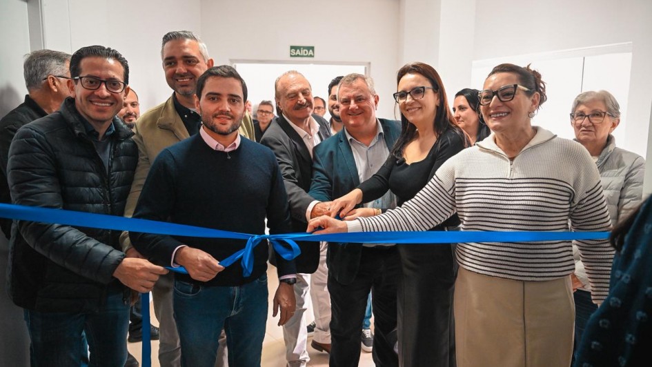 Grupo reunido em corredor de hospital corta uma fita azul em cerim&ocirc;nia de inaugura&ccedil;&atilde;o, com v&aacute;rias pessoas lado a lado em frente a paredes brancas e placa de sa&iacute;da ao fundo.