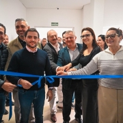Grupo reunido em corredor de hospital corta uma fita azul em cerim&ocirc;nia de inaugura&ccedil;&atilde;o, com v&aacute;rias pessoas lado a lado em frente a paredes brancas e placa de sa&iacute;da ao fundo.