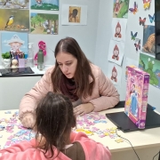 Sala de atendimento com decora&ccedil;&atilde;o infantil nas paredes, onde uma crian&ccedil;a e uma pessoa adulta montam um quebra-cabe&ccedil;a sobre uma mesa.
