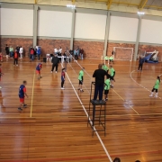 Foto mostra uma quadra de v&ocirc;lei onde acontece uma partida. Um time est&aacute; com camiseta verde claro, outro azul escuro. 