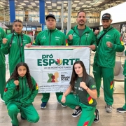 Foto mostra delega&ccedil;&atilde;o posando perfilados com a bandeira do Pr&oacute;-Esporte RS. O uniforme deles &eacute; verde com detalhes da bandeira do Rio Grande do Sul.