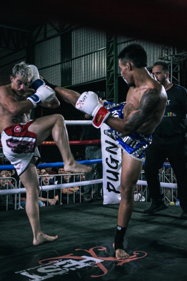 Foto mostra Rafael durante uma luta no ringue. Ele está dando um golpe com a perna na altura da cabeça do adversário.