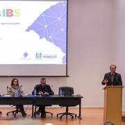 Foto mostra palestrante no p&uacute;lpito, no palco do evento, falando para a plateia.
