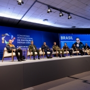 A imagem mostra um palco com oito palestrantes sentados diante de um painel onde se l&ecirc; "Congresso Internacional de Prote&ccedil;&atilde;o e Defesa Civil". 