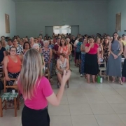 Foto mostra palestrante conduzindo atividade no sal&atilde;o cheio de mulheres. Todas est&atilde;o de p&eacute;.