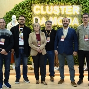 Seis pessoas posam para a foto em frente a um painel verde com as palavras "Cluster da Moda" em destaque. 