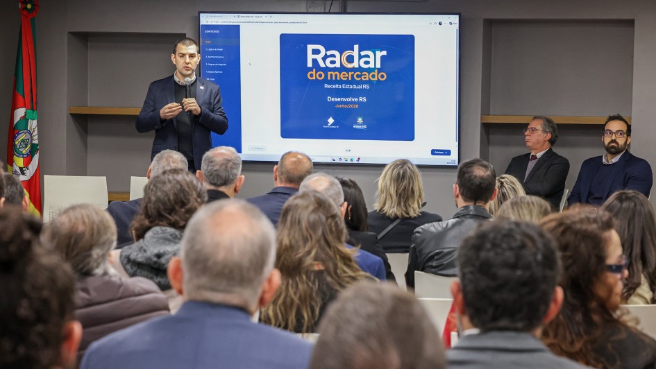 Foto mostra um dos respons&aacute;veis pelo programa apresentando a iniciativa, diante da plateia. 