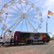 Foto mostra a unidade do Tudo F&aacute;cil no p&aacute;tio do Acampamento Farroupilha. Ao fundo, aparece a roda gigante. O c&eacute;u est&aacute; azul.
