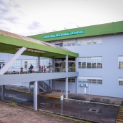 Foto mostra a fachada do Hospital Regional de Santa Maria. Na frente da institui&ccedil;&atilde;o h&aacute; uma passarela com telhado verde. A mesma cor est&aacute; na faixa no alto do pr&eacute;dio. 