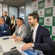 Reuni&atilde;o em ambiente institucional, com participantes sentados &agrave; mesa diante de um painel com os logotipos do Governo do Estado e da Comiss&atilde;o de Transi&ccedil;&atilde;o. Sobre a mesa h&aacute; documentos, dispositivos eletr&ocirc;nicos e materiais de trabalho utilizados durante o encontro.