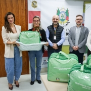 Foto mostra secret&aacute;rios e coordenadoras com kits. Os kits s&atilde;o bolsas verdes. Duas mulheres seguram um dos kits que est&aacute; dentro de uma banheira branca de beb&ecirc;.
